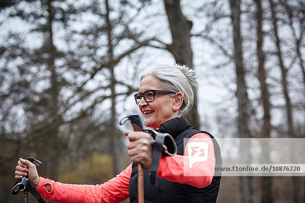 Reife Frau trainiert im Park  stehend mit Nordic-Walking-Stöcken