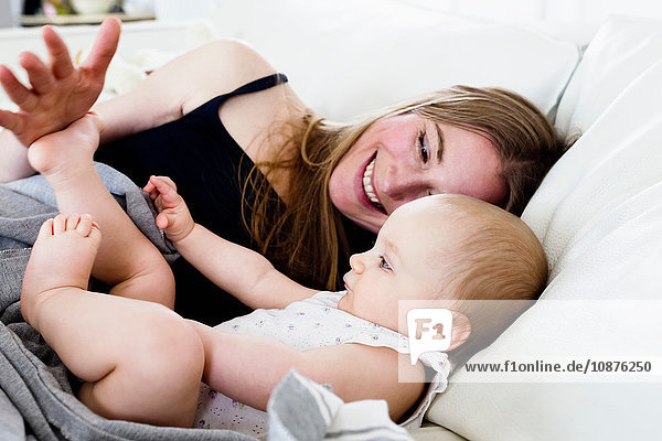 Mid adult woman playing with baby daughters bare feet on sofa