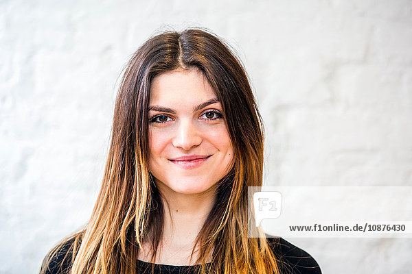 Head and shoulder portrait of beautiful young woman in front of white wall