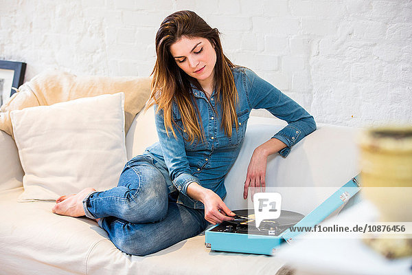 Young woman sitting on sofa listening to vintage record player