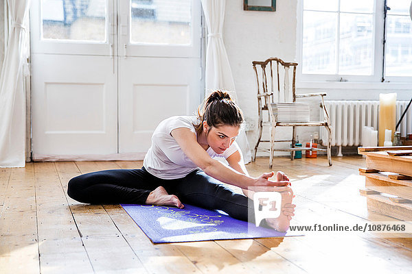 Junge Frau praktiziert Yoga  berührt Zehen in Wohnung