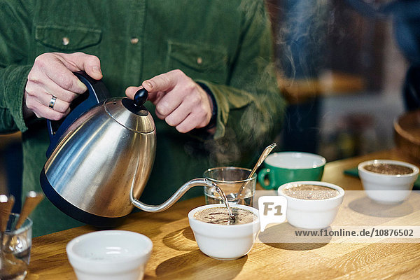 Mann gießt kochendes Wasser in Kaffeeschüsseln zur Verkostung auf der Kaffeetheke