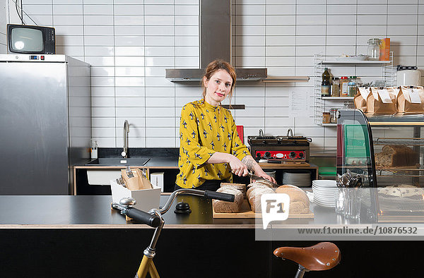 Portrait of waitress slicing bread at counter of hipster bike repair cafe