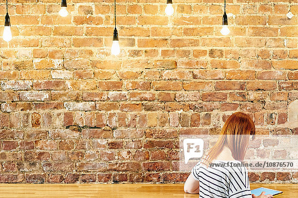 Weibliche Kundin sitzt an Backsteinwandbank und blättert auf digitalem Tablet im Café