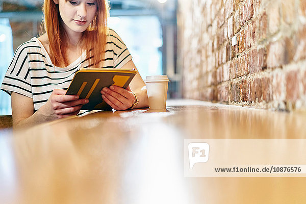 Junge Frau sitzt auf Bank und blättert auf digitalem Tablet im Café