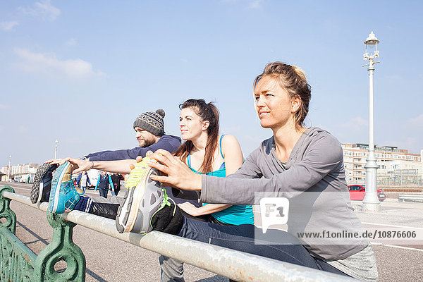 Drei Läufer und Läuferinnen wärmen sich am Strand von Brighton auf und berühren die Zehen