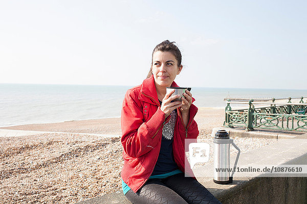 Läuferin macht eine Kaffeepause an der Wand am Strand von Brighton Beach