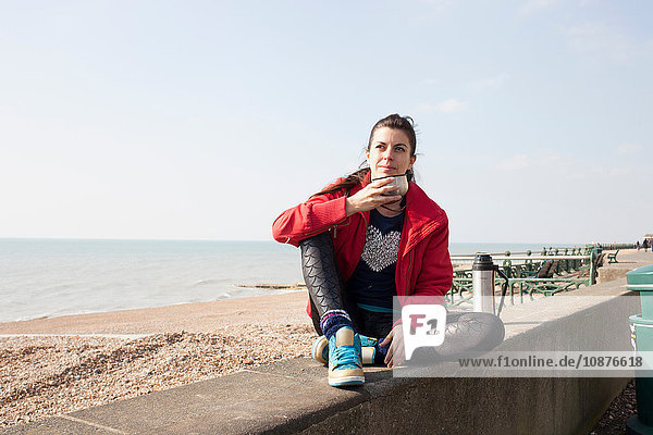 Läuferin macht eine Kaffeepause an der Wand am Strand von Brighton Beach