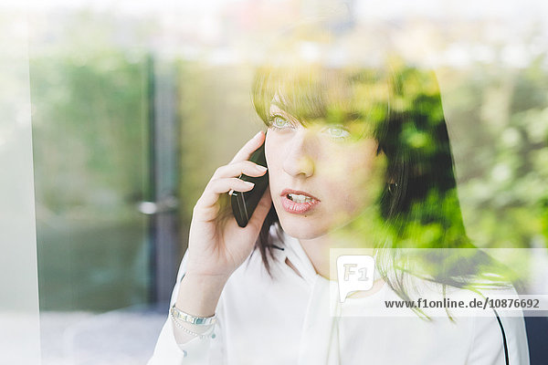 Fensteransicht einer jungen Geschäftsfrau  die auf einem Smartphone spricht