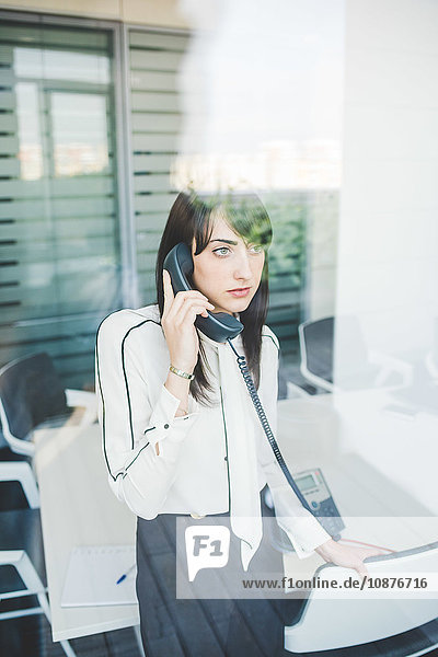 Office window view of young businesswoman talking on landline