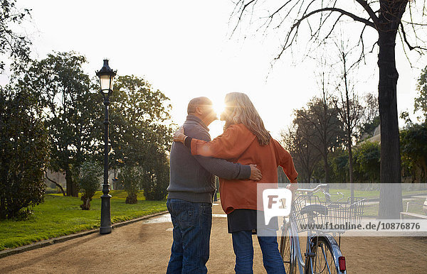 Couple on tree lined path holding bicycle kissing