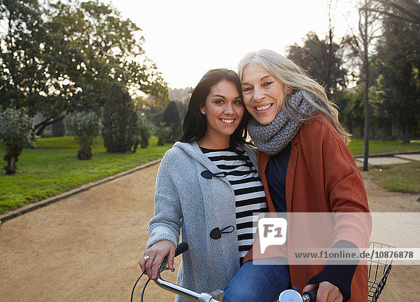 Mutter und erwachsene Tochter im Park mit Fahrrad  die lächelnd in die Kamera schauen