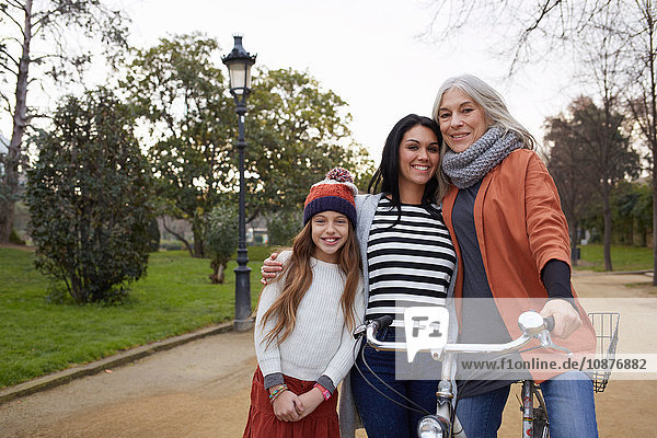 Mother and daughter and grandmother in park with bicycle looking at camera smiling