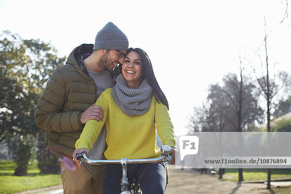 Mid adult man hugging smiling mid adult woman on bicycle in park