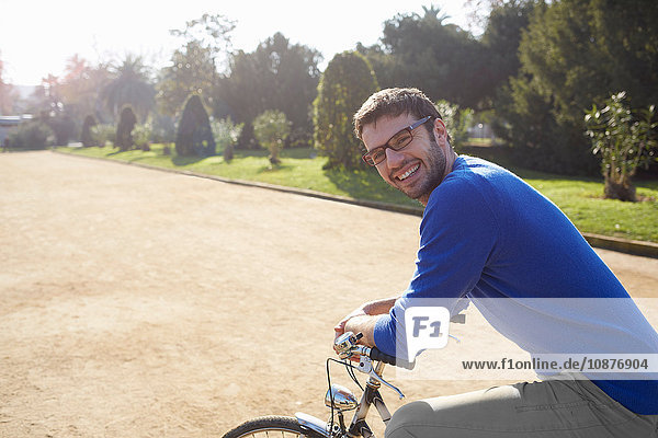 Mittelgroßer erwachsener Mann sitzt auf einem Fahrrad im Park und schaut lächelnd in die Kamera