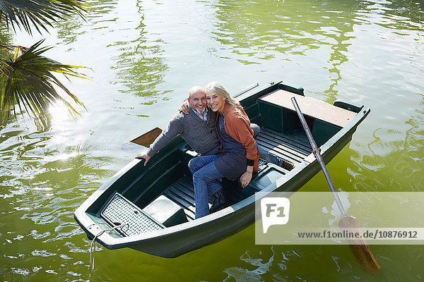 Paar im Ruderboot auf dem See umarmt sich und schaut lächelnd in die Kamera