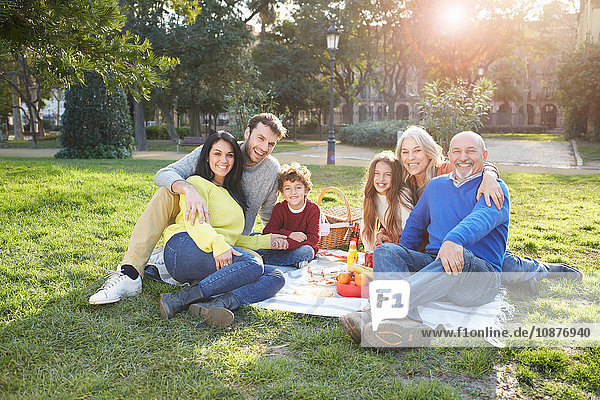Multi generation family sitting on grass having picnic  looking at camera smiling