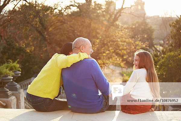 Rückansicht eines Mannes  der mit Tochter und Enkelin auf einer Stufe im Park sitzt