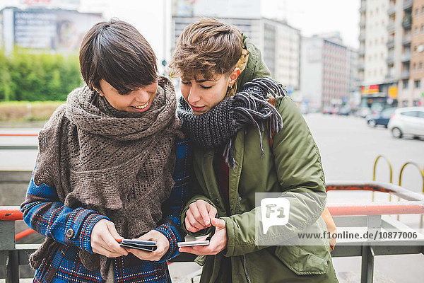 Zwei Schwestern beim Blick auf das mobile Smartphone  lächelnd  im Freien