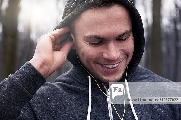 Junger Mann im Freien  trägt Kapuzenpulli und Kopfhörer  lächelt
