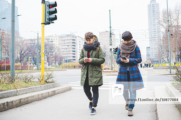 Two sisters walking along street  using smartphones