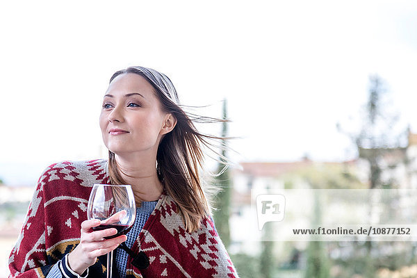 Frau hält ein Glas Rotwein und schaut lächelnd weg