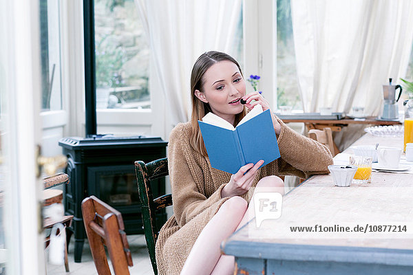 Frau sitzt am Esstisch und isst Brombeeren und liest Buch