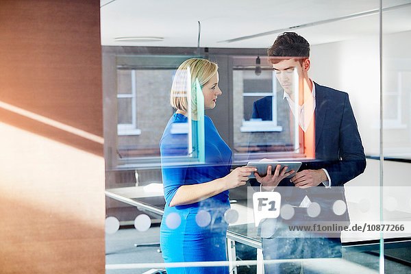 View through glass partition of colleagues holding digital tablet