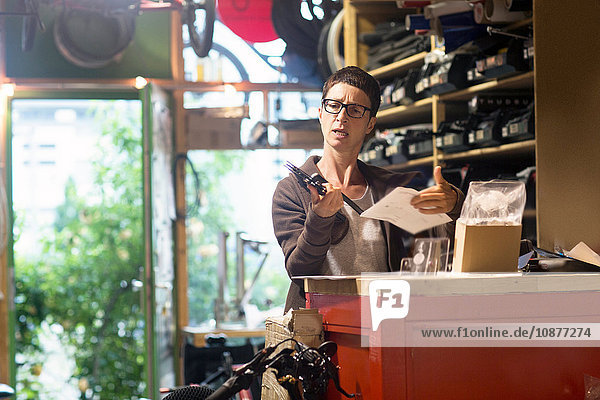 Woman at counter in bicycle workshop holding bike part and paperwork