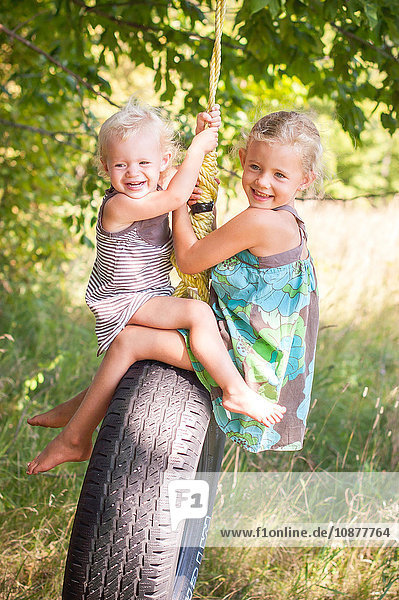 Weibliches Kleinkind und Schwester spielen einander gegenüber auf Reifenschaukel