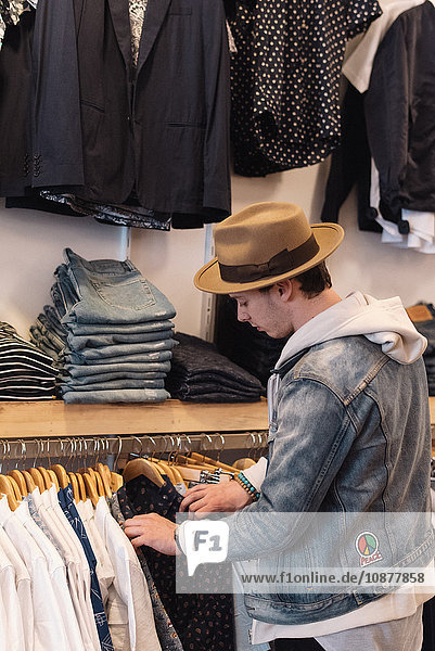 Junger Mann durchsucht Hemden auf dem Regal  im Kleiderladen