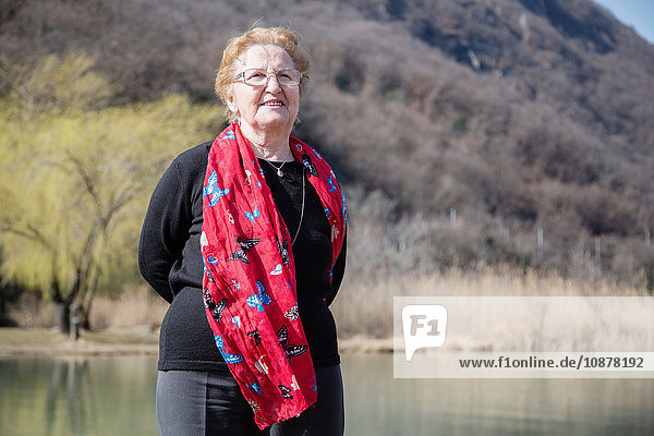 Senior woman wearing scarf in front of lake looking at camera smiling