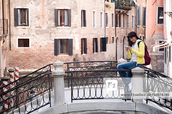 Junge Frau sitzt auf Kanalbrücke und betrachtet Digitalkamera  Venedig  Italien