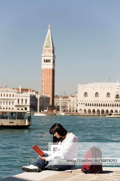 Junge Frau beim Lesen eines Reiseführers am Hafen gegenüber dem Markusplatz  Venedig  Italien