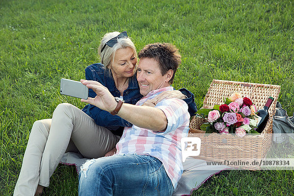 Mature couple on grass having picnic  taking selfie