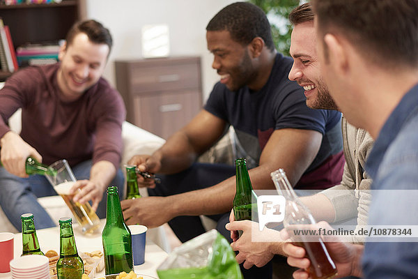 Gruppe von Männern sitzt im Salon und hält Bierflaschen lächelnd in der Hand