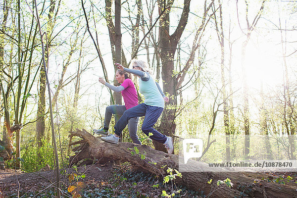 Side view of women in forest jumping over fallen tree