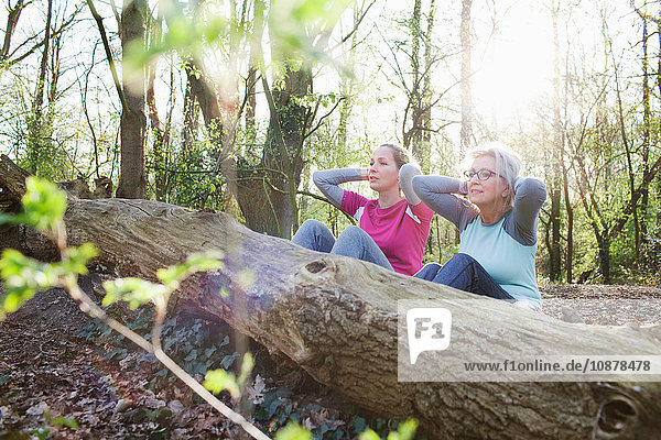 Women in forest hands behind head doing sit up against fallen tree