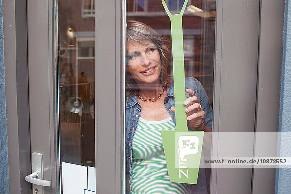 View through glass shop door of woman holding open sign