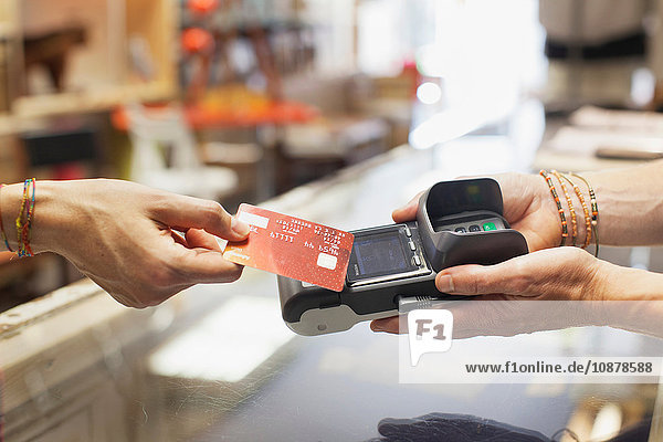 Schrägansicht der Hand einer Frau  die eine Kreditkarte benutzt  um kontaktlos an einem Chip- und Pin-Automaten zu bezahlen