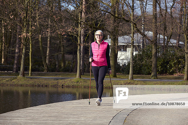 Vorderansicht einer Nordic-Walking-Frau am Teich in voller Länge