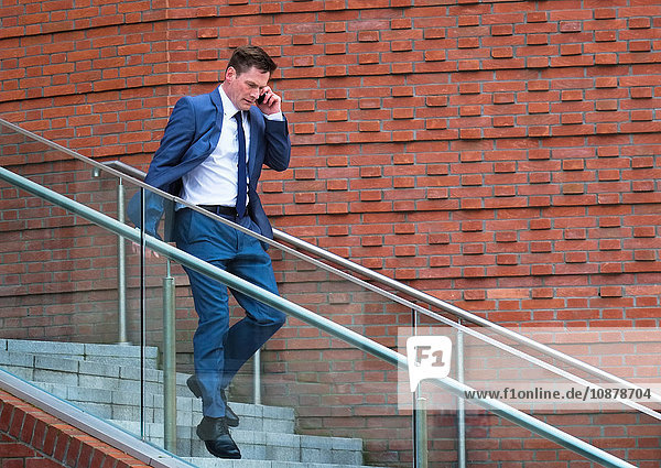 Ein reifer Geschäftsmann geht eine Treppe hinunter und benutzt ein Smartphone
