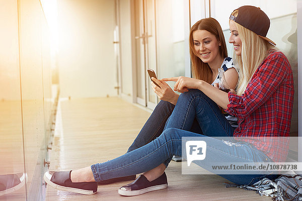 Two female friends  sitting outdoors  looking at smartphone