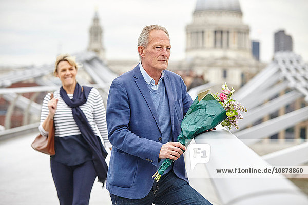 Reifer Mann mit Blumenstrauss wartet vor dem Datum auf der Millennium Bridge  London  UK