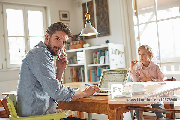 Father on phone while working in home office with son