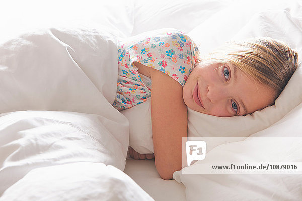 Porträt eines blondhaarigen Mädchens  das im Bett ein Kissen umarmt
