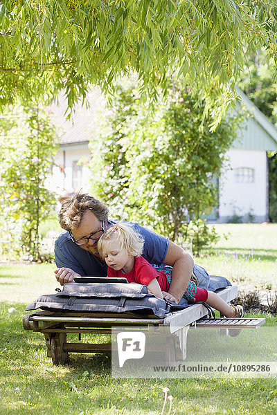 Sweden Skane Mossby Daughter with father lying on deckchair and using tablet pc