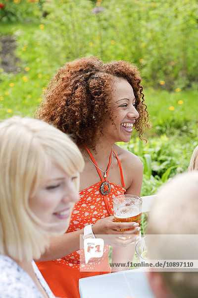 Frau mit lockigen Haaren sitzt am Picknicktisch mit einem Glas Bier