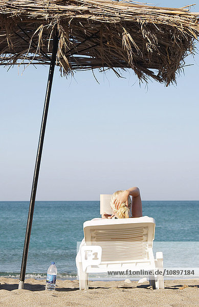 Griechenland  Karpathos  Frau beim Sonnenbaden und Lesen am Strand