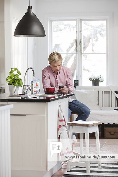 Schweden Teenage boy (16-17) texting in der Küche